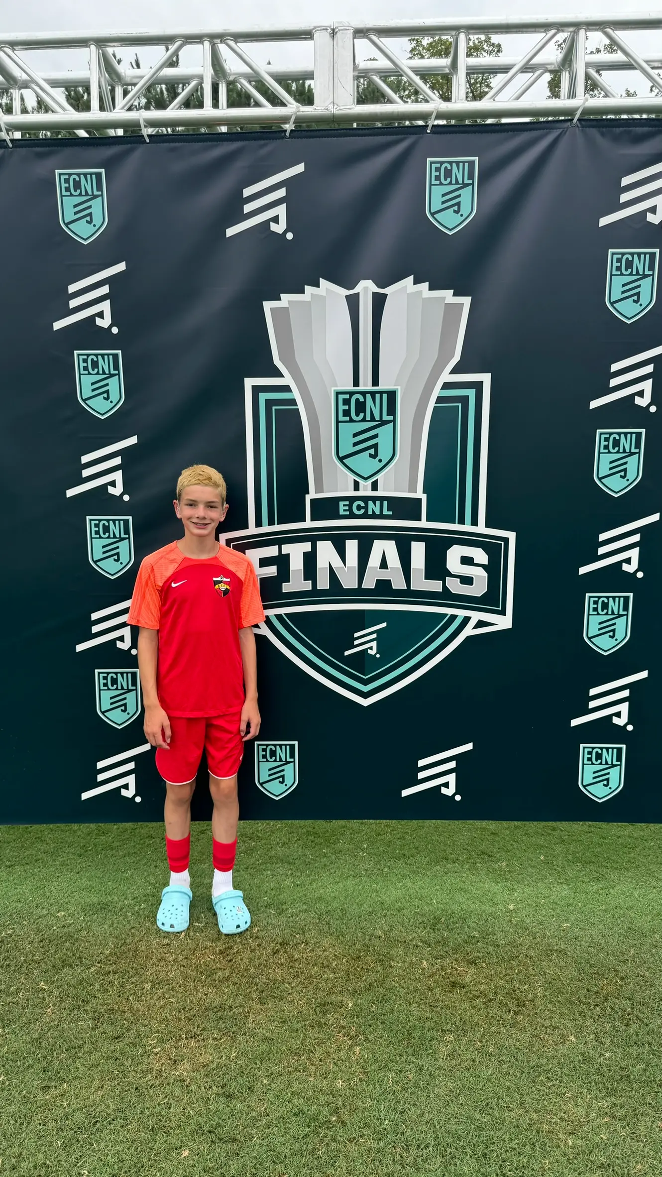Daylen Hammon in orange Real Colorado kit standing in front of ECNL Finals step-and-repeat backdrop