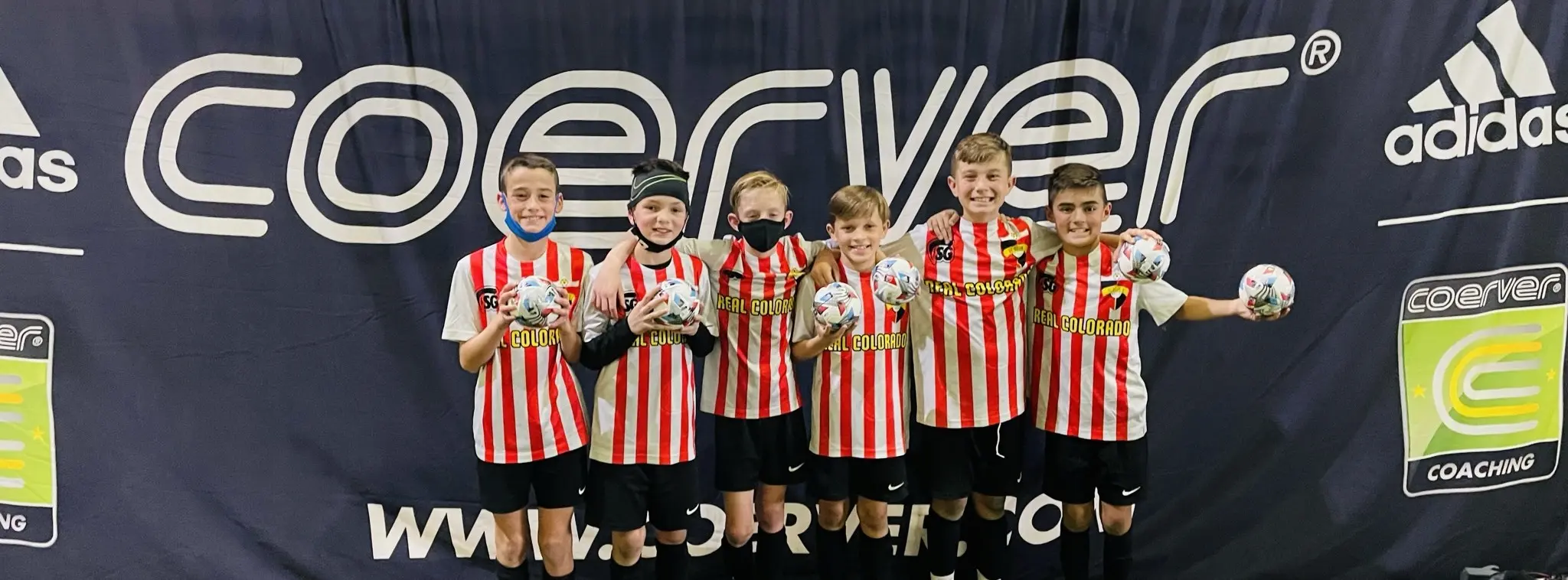 Real Colorado Academy players in red and white striped kits holding adidas balls in front of Coerver Coaching banner