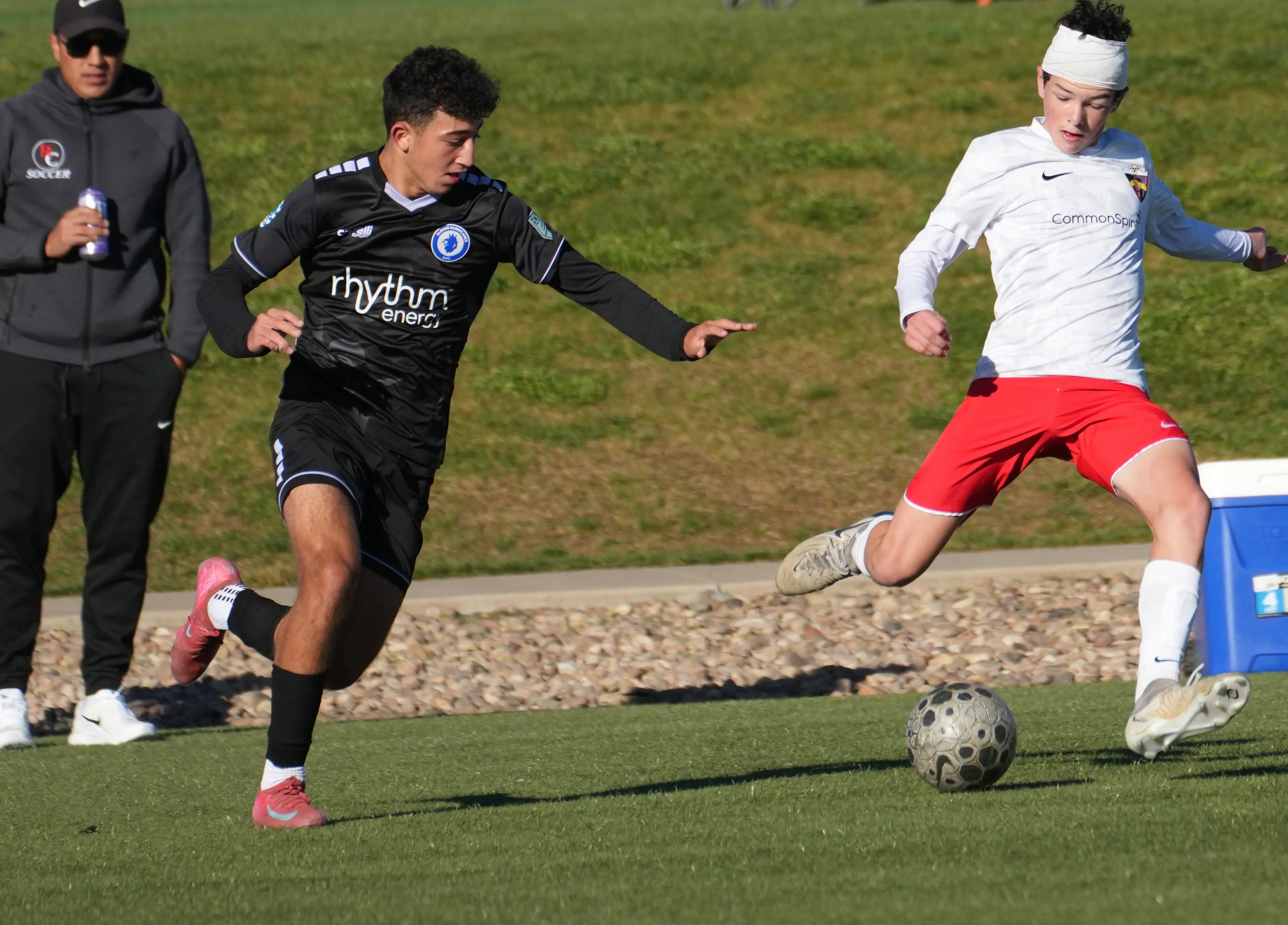 Daylen Hammon in white Real Colorado CommonSpirit kit with white headband cutting past opponent in black Rhythm Energy kit during MLS Next match