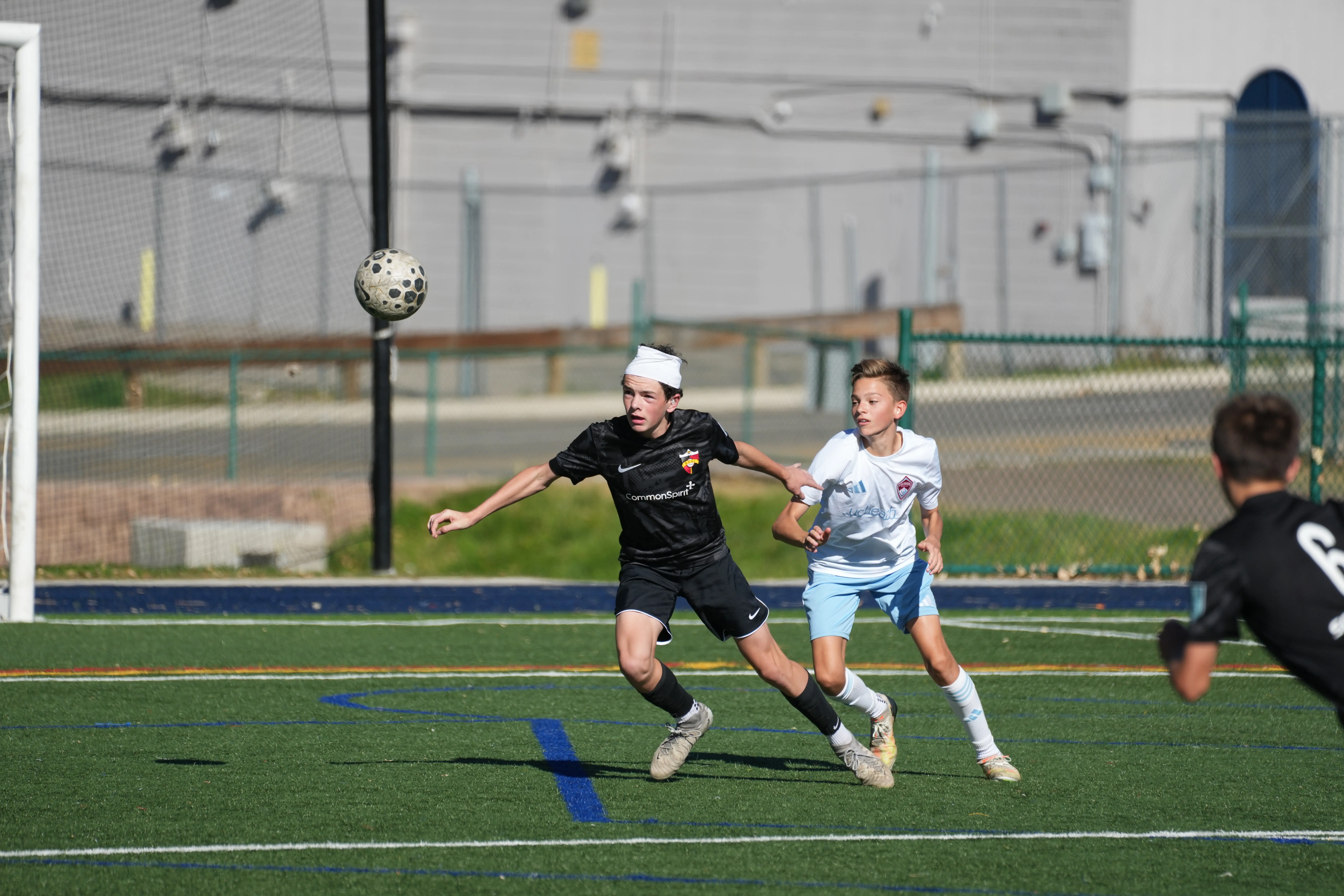 Daylen Hammon in black Real Colorado CommonSpirit kit with white headband chasing ball vs Colorado Rapids white kit player during MLS Next match