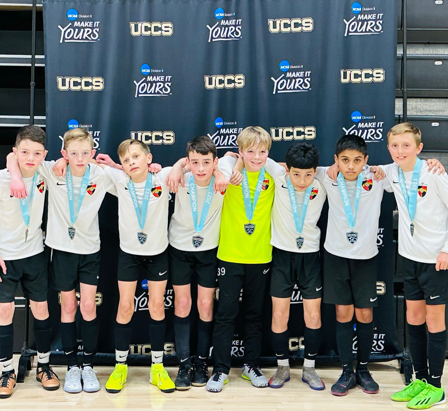 Real Colorado Academy Kick It 3v3 Champions — players with blue medals in front of Kick It 3v3 inflatable
